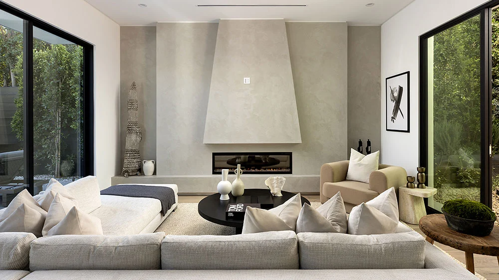 Modern living room with sculptural stone fireplace wall, floor-to-ceiling black-framed windows, and neutral furnishings